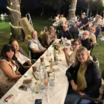 Gruppi di amici seduti sull’erba, circondati da luci decorative, mentre condividono cibo e bevande.