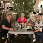 Gruppi di amici seduti sull’erba, circondati da luci decorative, mentre condividono cibo e bevande.