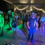 Scorcio di una festa con musica, balli e ospiti vestiti in stile country.
